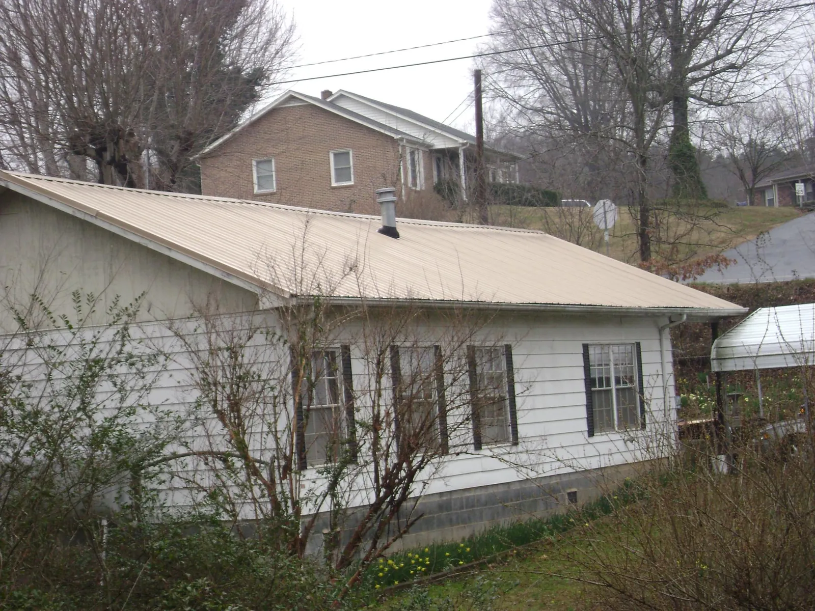 Tan metal roof on a white sided house set into a hillside — Commercial Roofing by Roofing Brothers in Ventnor City
